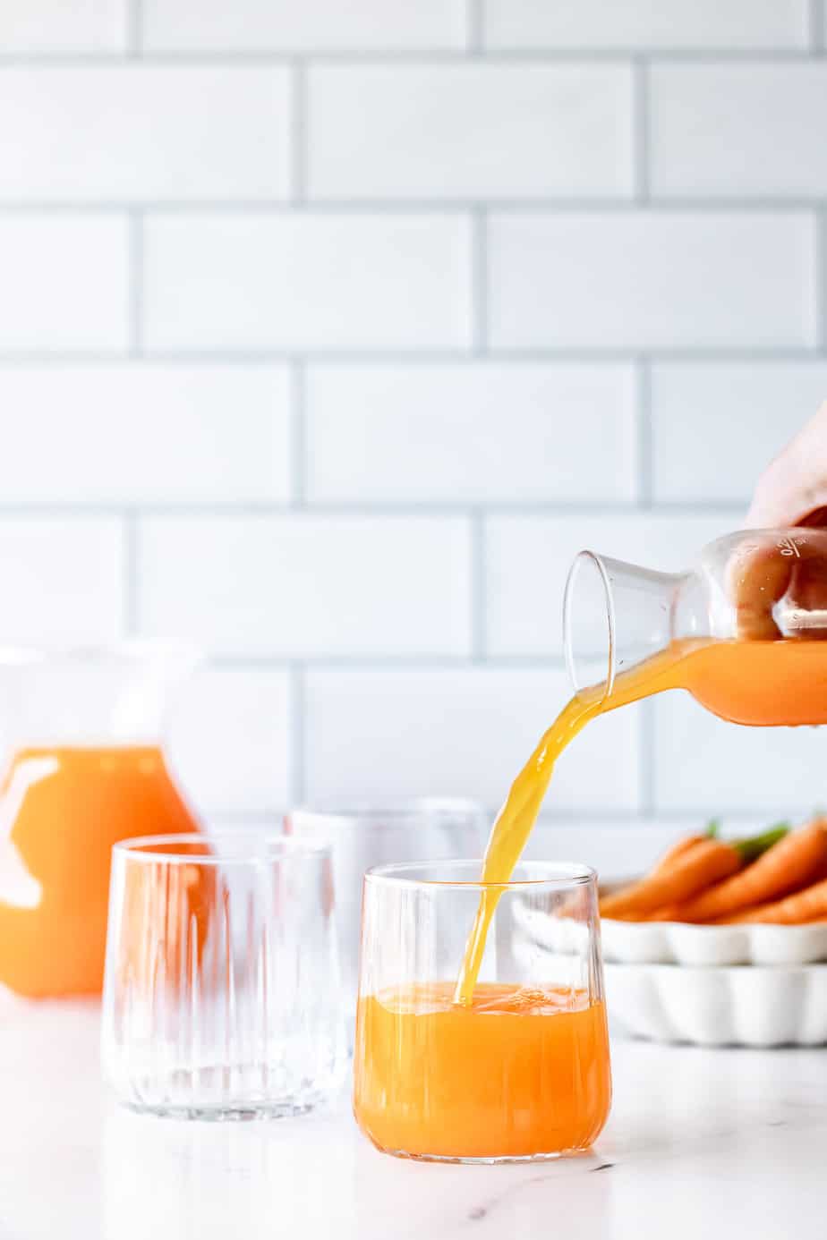 A jug pouring carrot juice into a serving glass