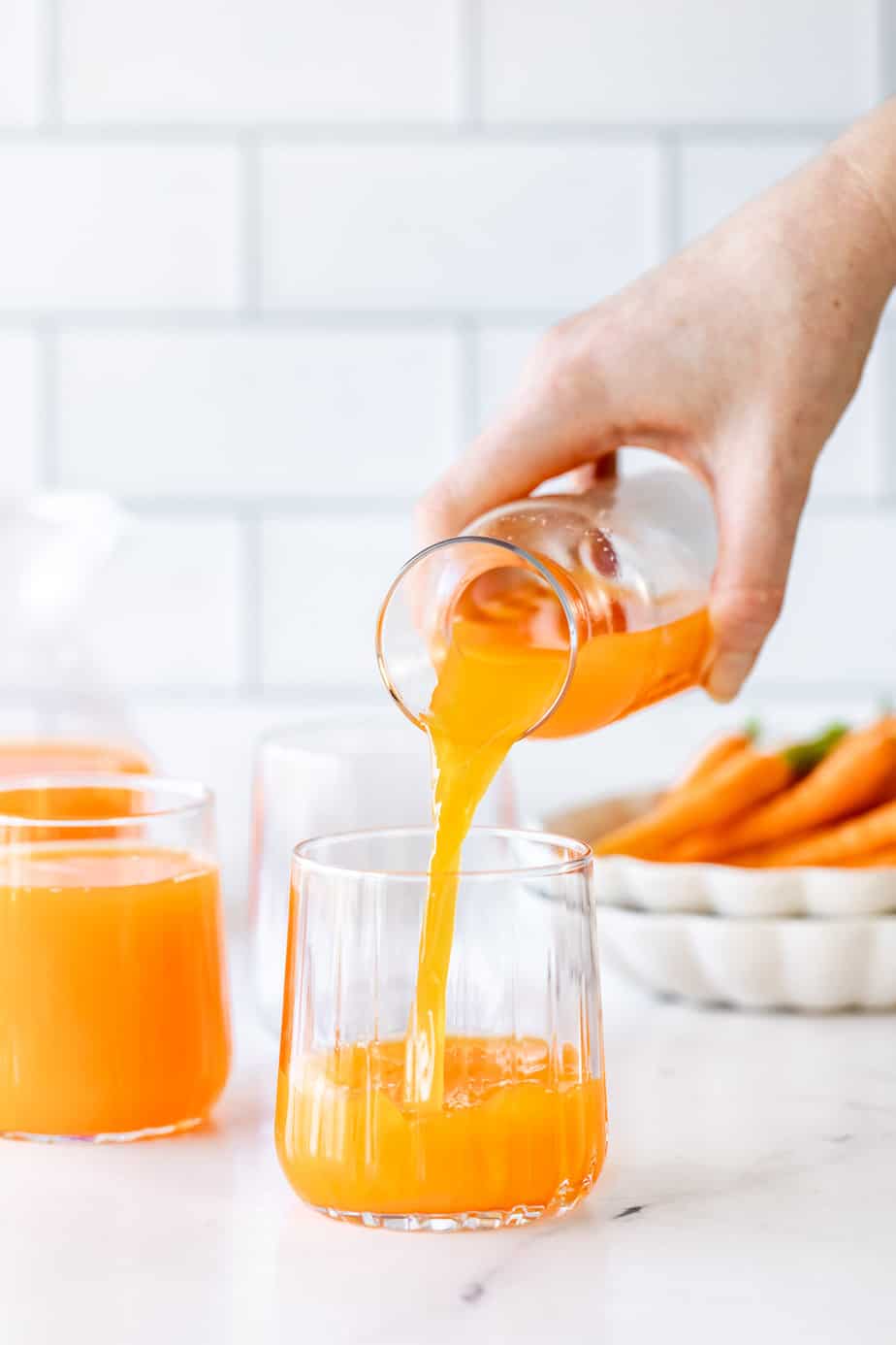 two glasses of carrot juice on a marble counter.