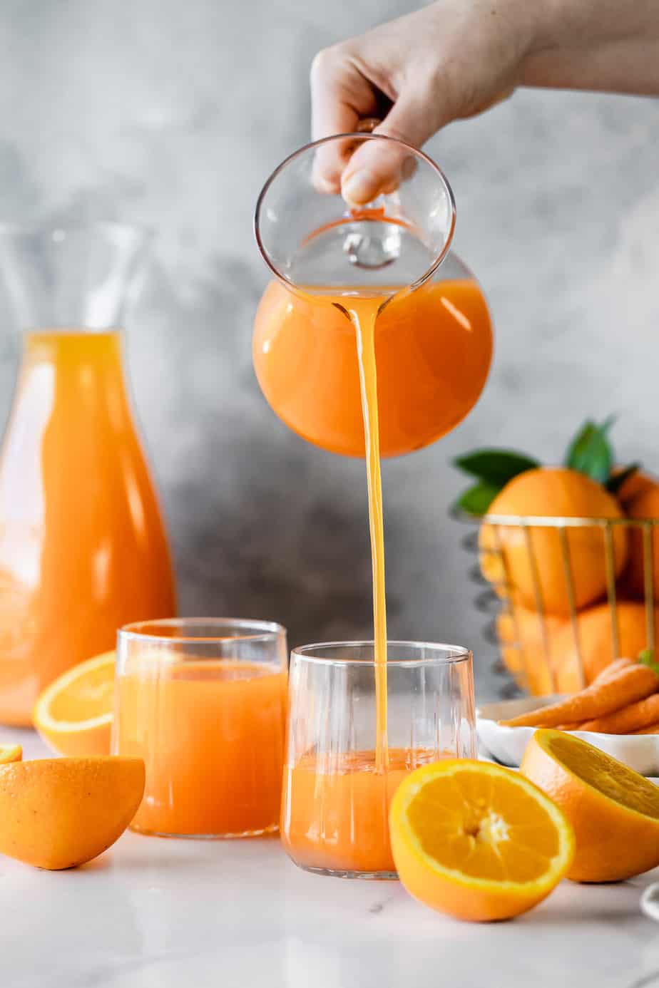 A jug pouring orange breakfast juice into serving glasses.