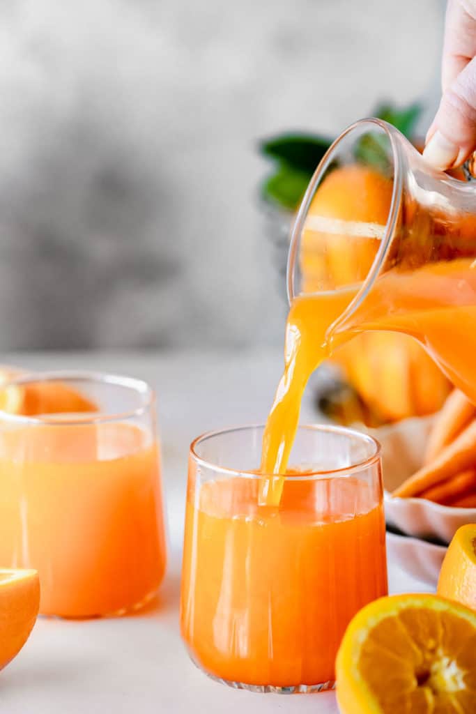 carrot and orange juice in a glass with fresh oranges