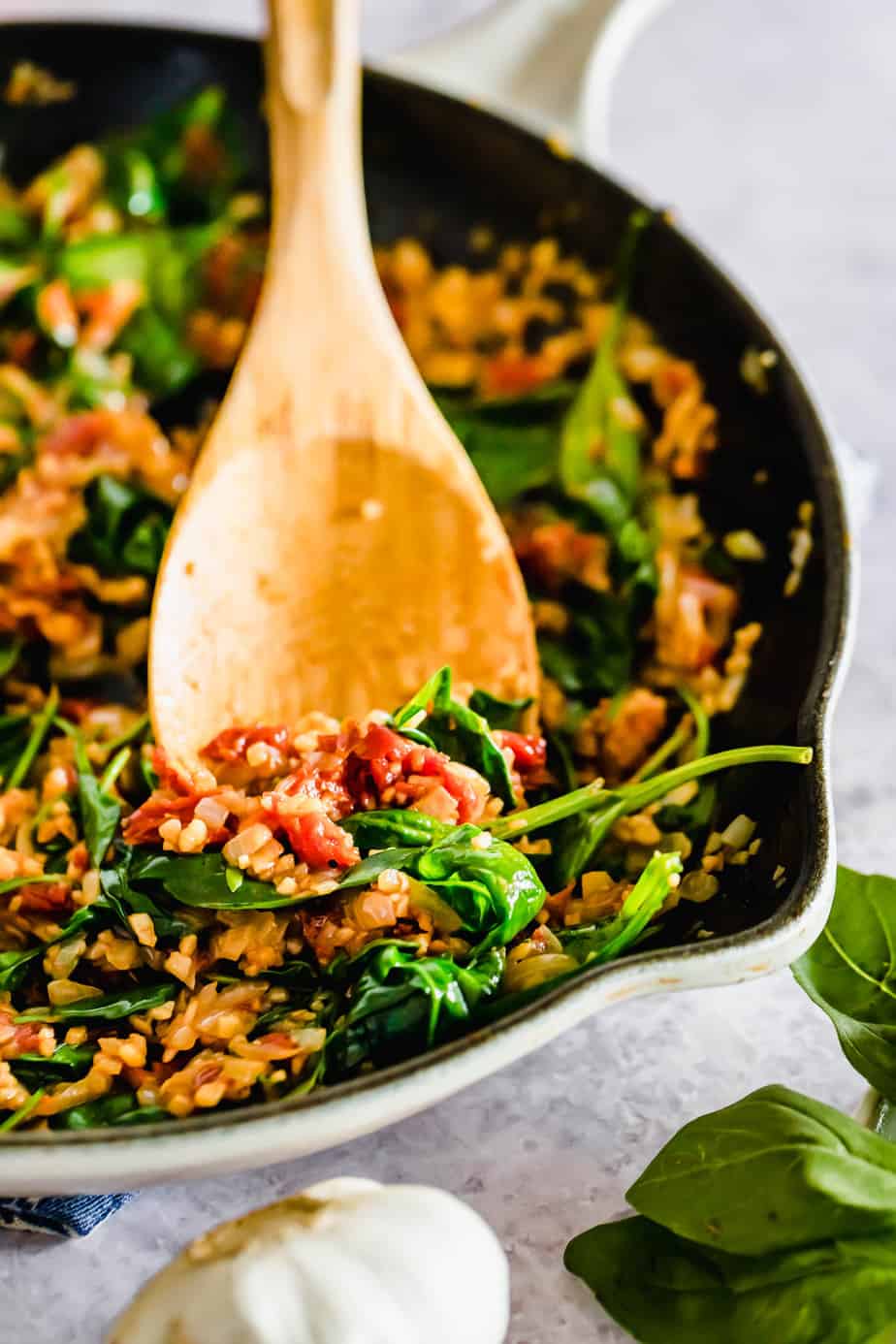 Cooked spinach and vegetables in a skillet with wooden spoon.