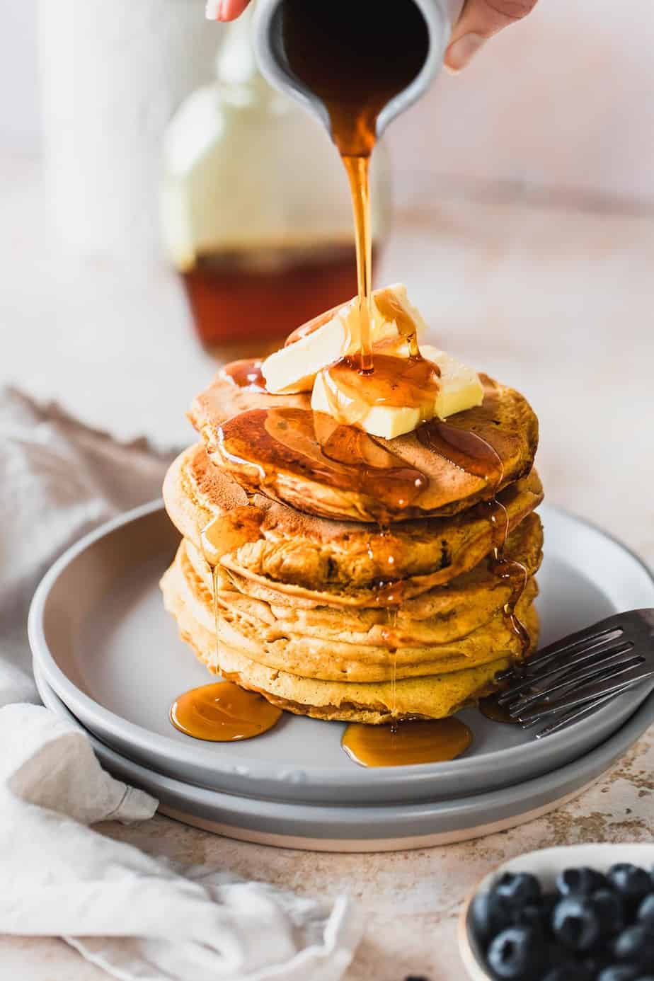 A jug pouring maple syrup over pumpkin pancakes.