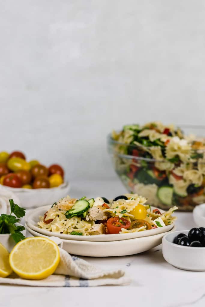 pasta salad in white bowl with lemons and tomatoes