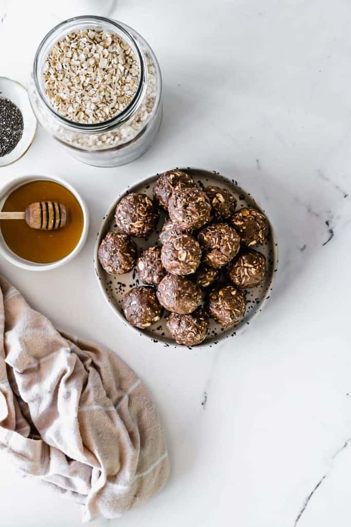 A plate of chocolate energy balls with a small bowl of honey.