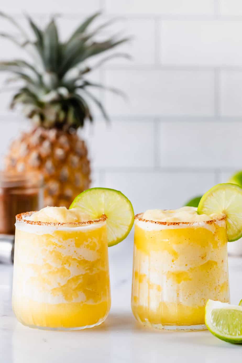 Two Spicy Frozen Pineapple Margaritas in serving glasses with lime slices.
