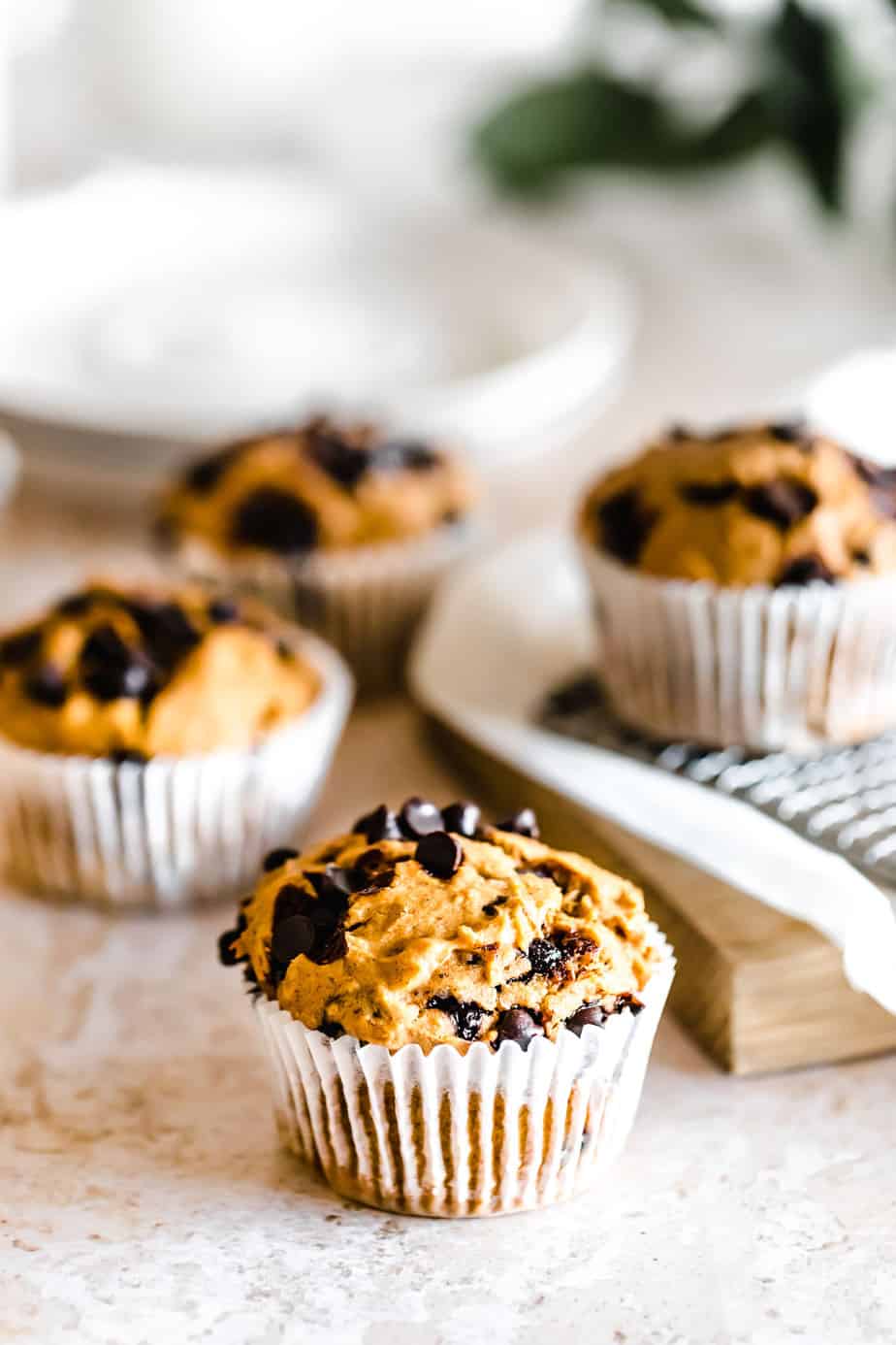 Pumpkin Banana Chocolate Chip Muffins in white paper liners topped with choc chips.