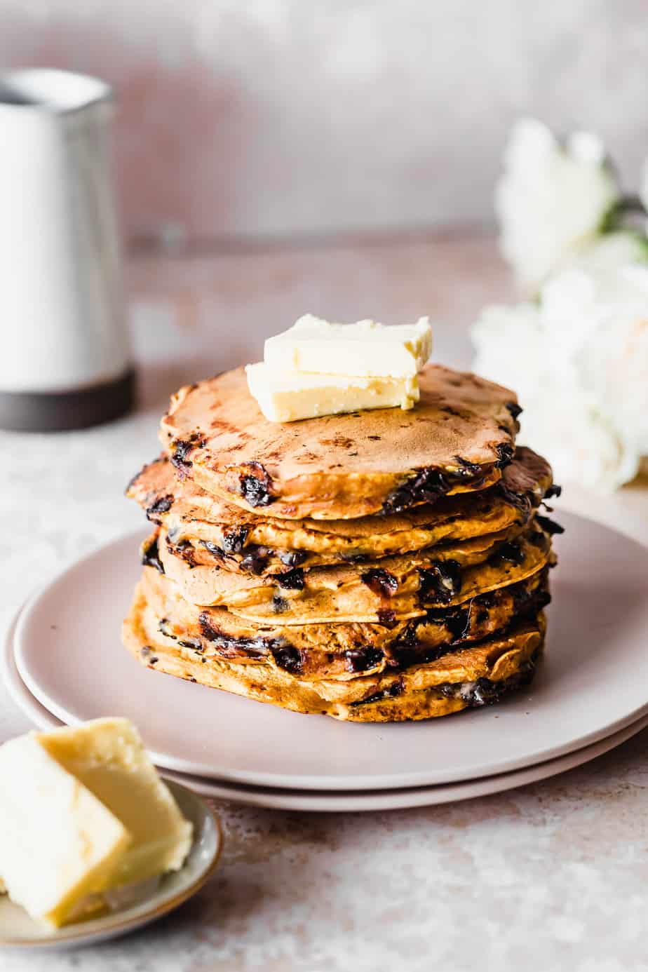 A stack of pumpkin chocolate chip pancakes topped with butter sitting on a plate.