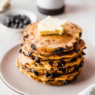 A stack of pumpkin chocolate chip pancakes topped with butter served on a plate.