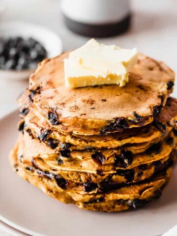 A stack of pumpkin chocolate chip pancakes topped with butter served on a plate.