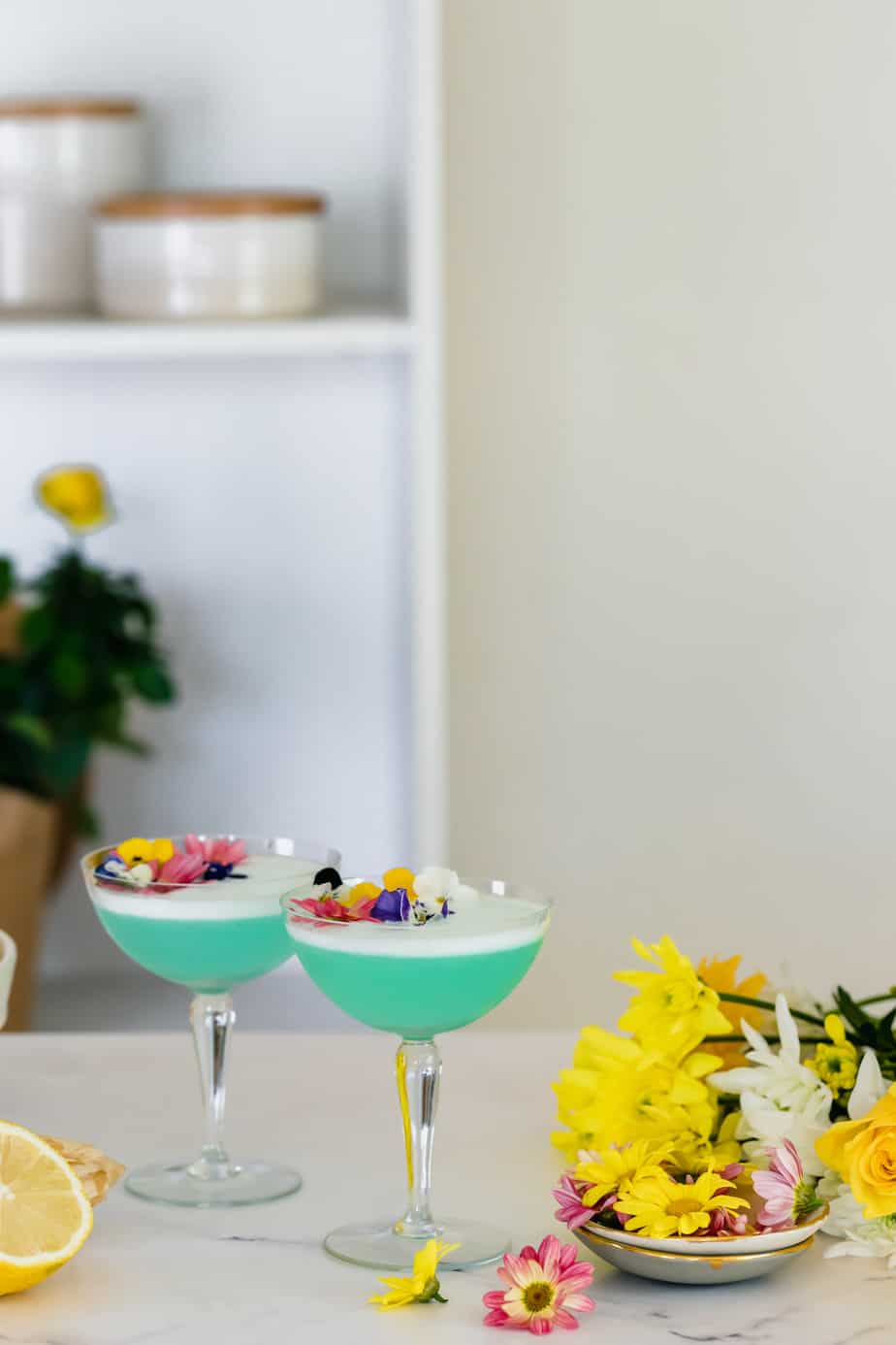 Two blue cocktails in serving glasses and fresh flowers.