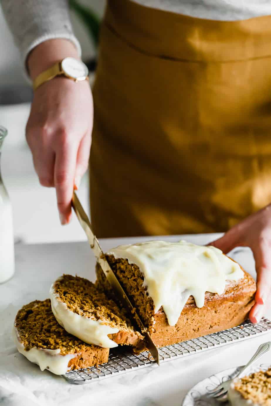 A golden knife slicing through a pumpkin bread topped with cream cheese frosting.
