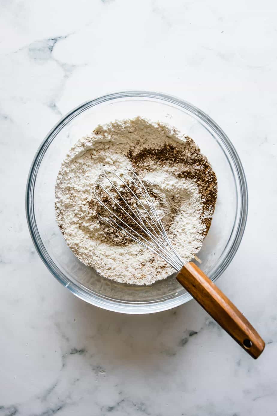 Dry ingredients mixed in a glass bowl with a whisk.