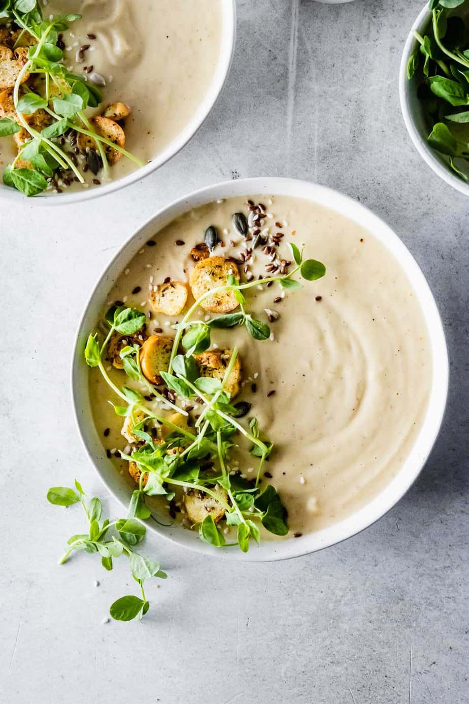 A bowl of creamy soup with fresh herbs and microgreens on top.