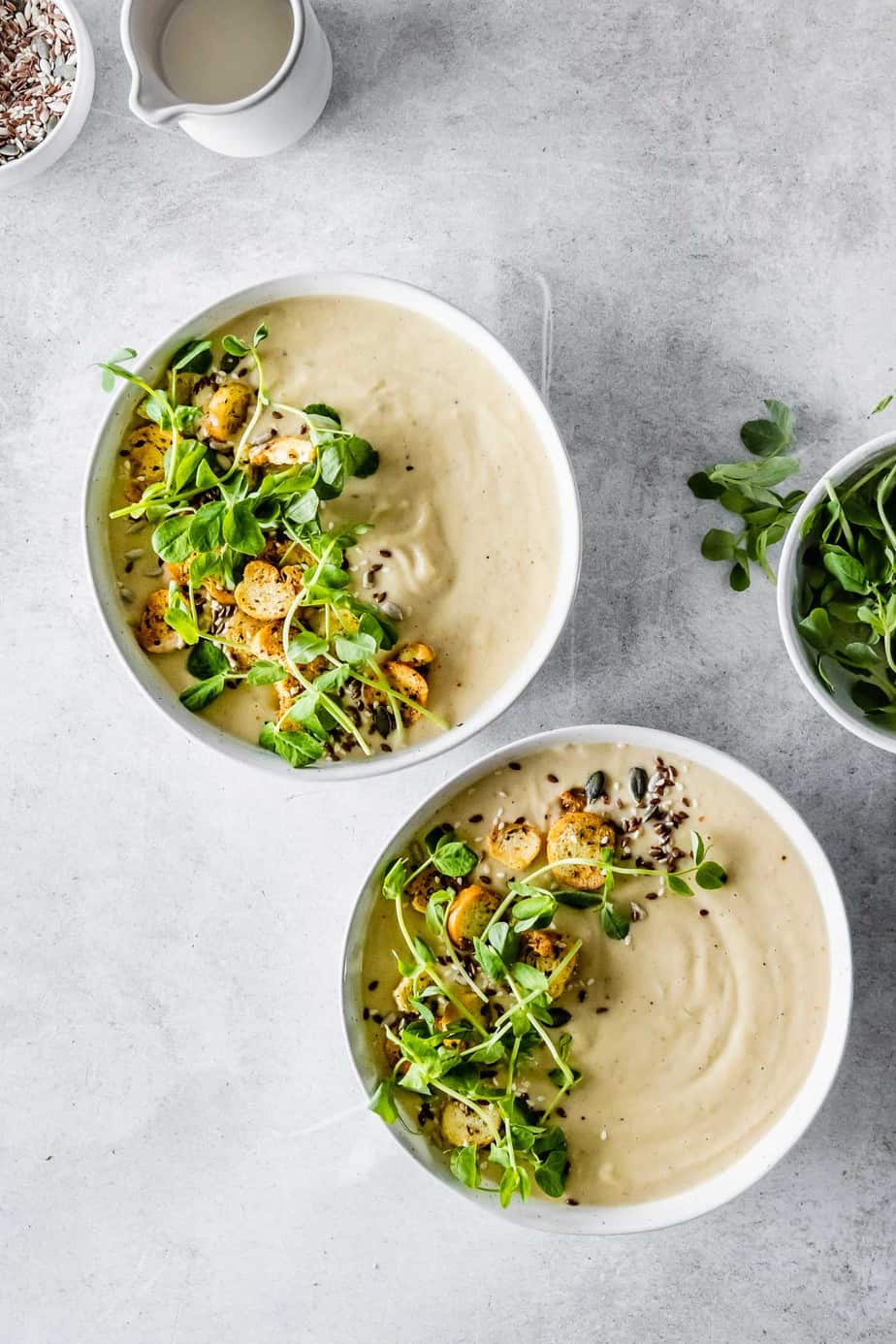 Soup in white bowls garnished with seeds and pea shoots.