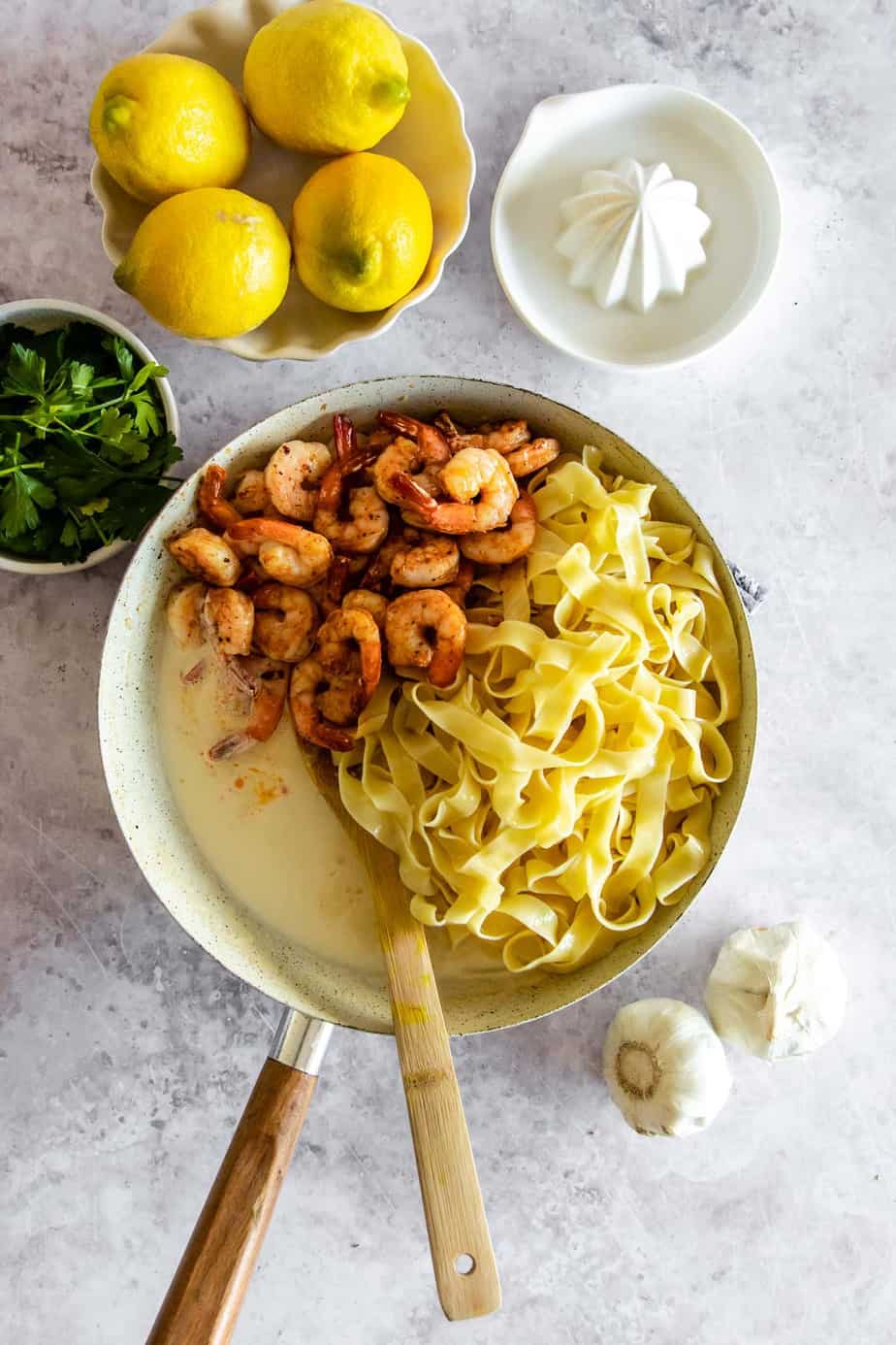 Pasta, shrimp, and cream sauce in a skillet with a wooden spoon.