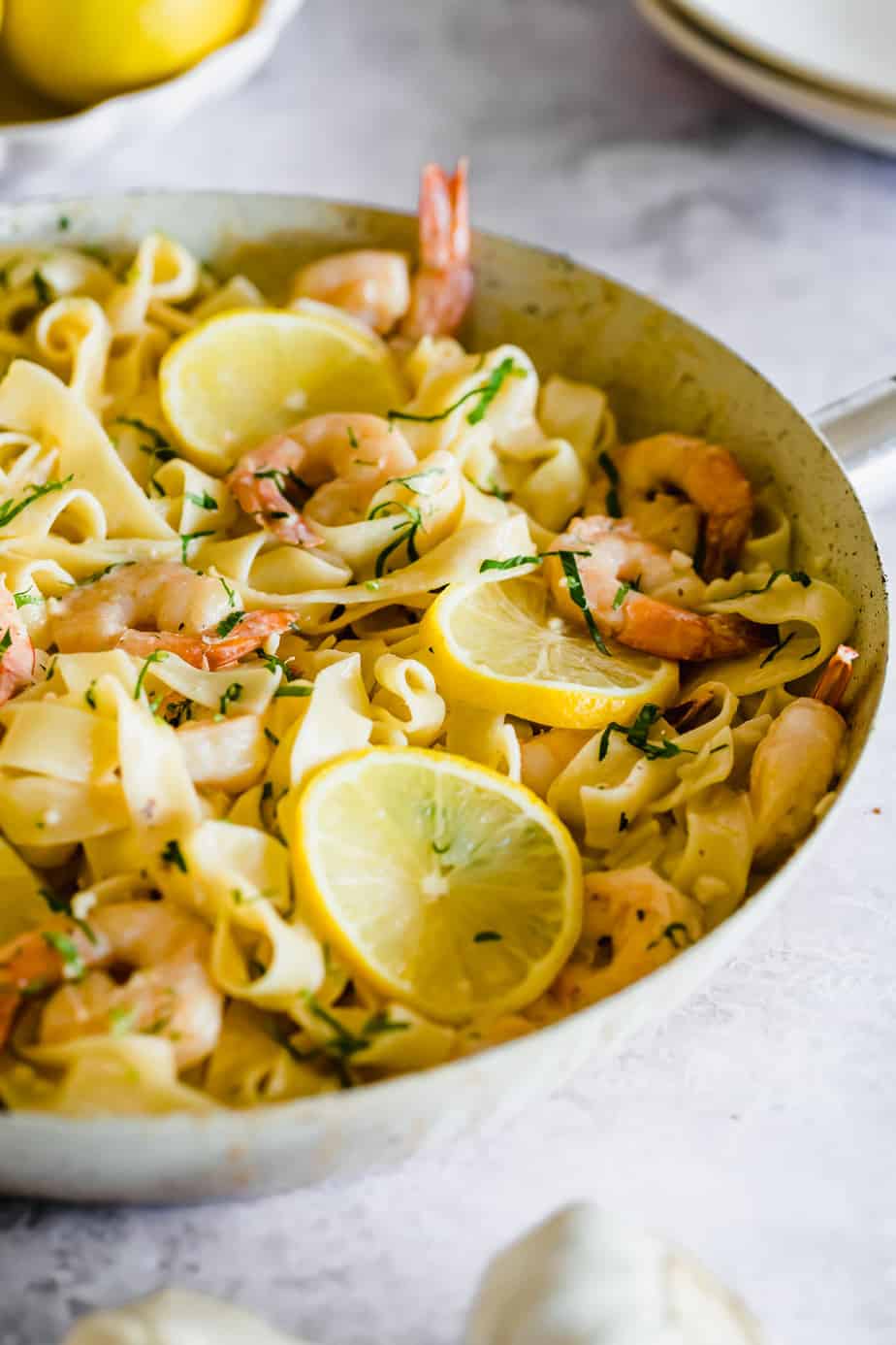 A skillet with pasta coted in cream and herbs with lemon and shrimp.