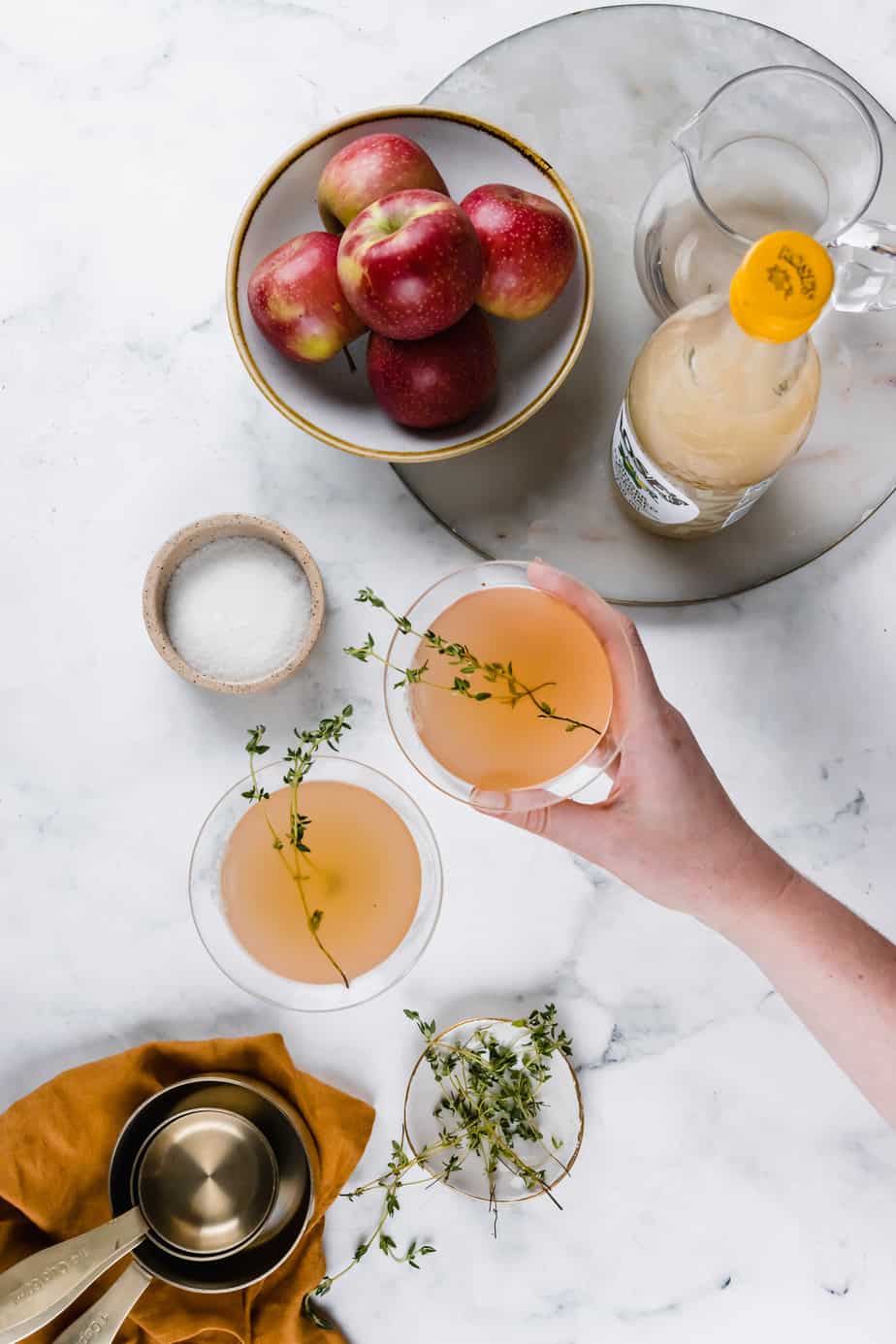 A hand holding a spiced apple cocktail with fresh thyme.