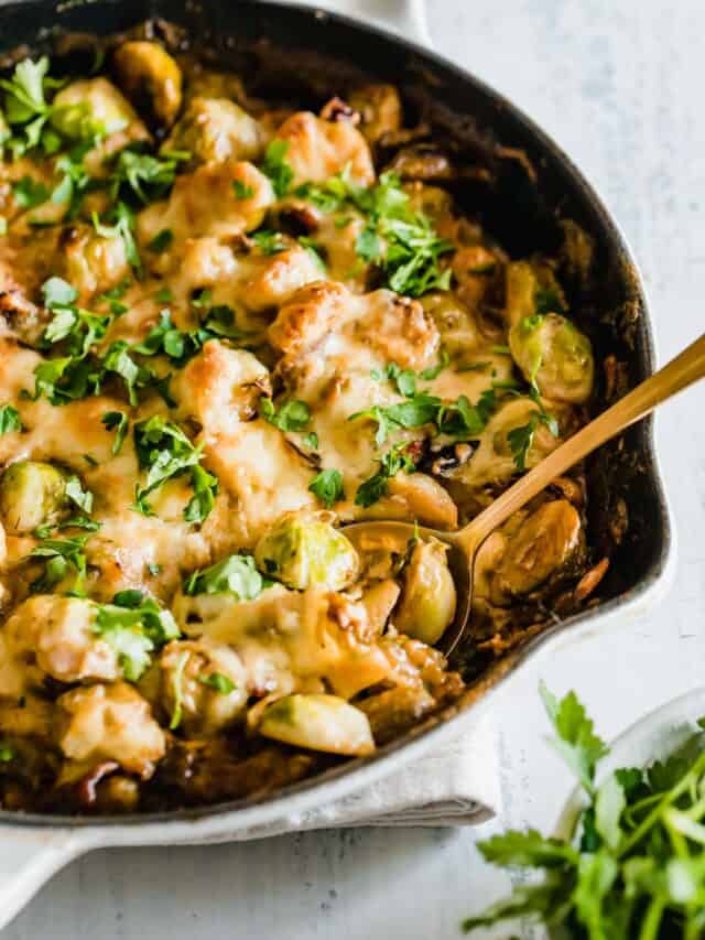 brussels sprouts in a white and black cast iron pan with cheese and fresh herbs