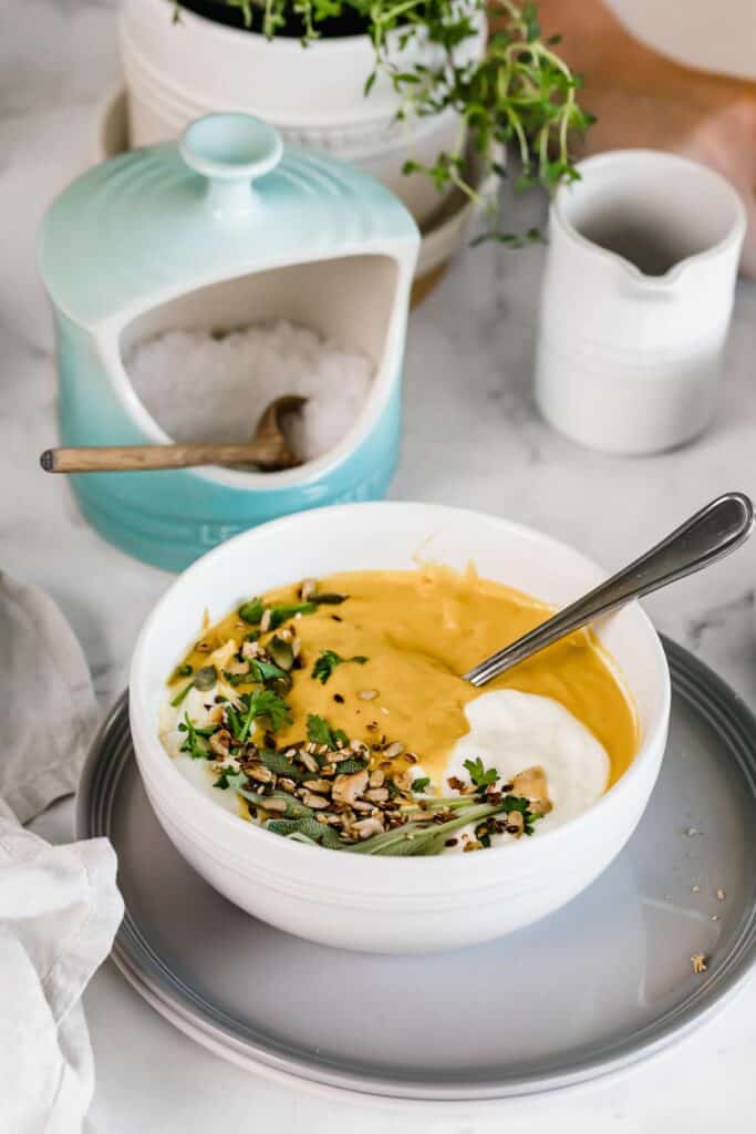 Bowl of pumpkin lentil soup with seeds and fresh herbs as garnish.