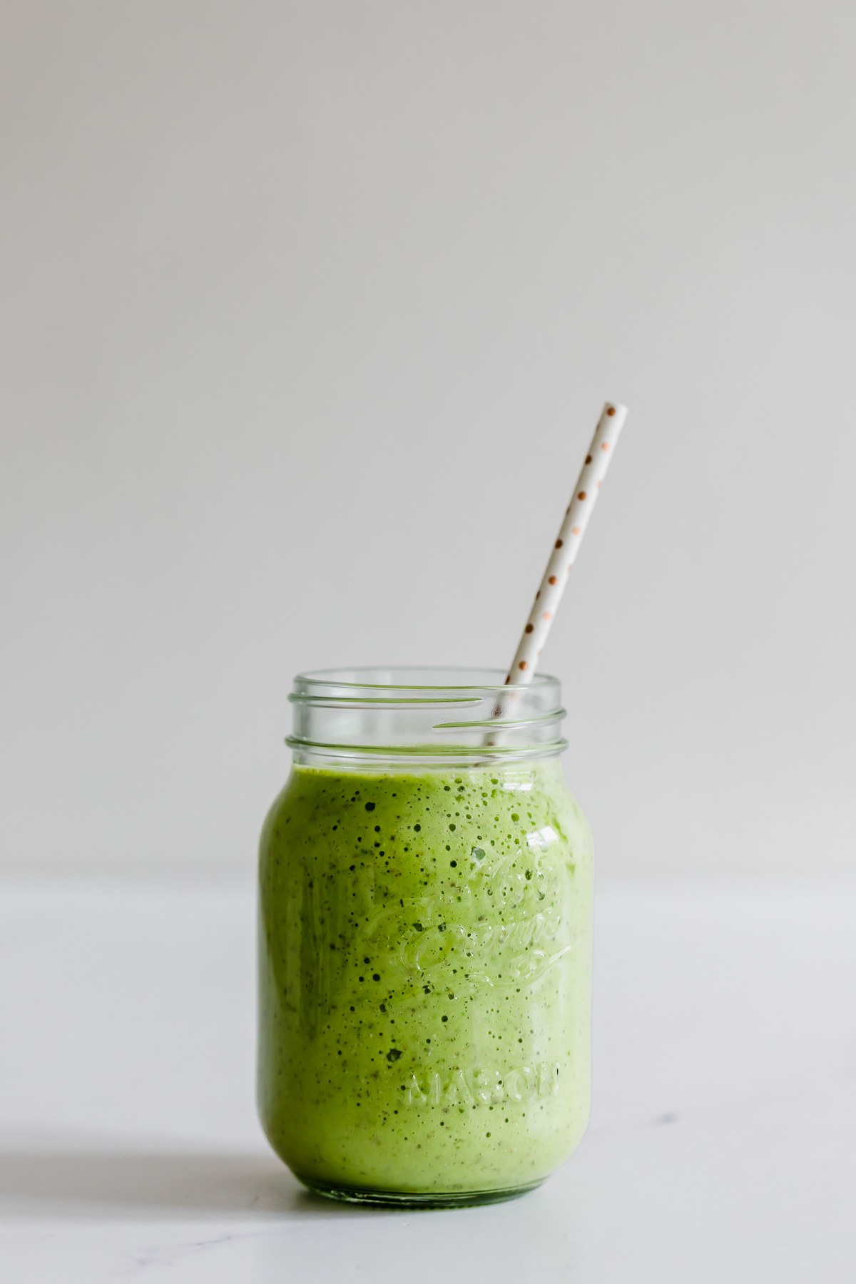 pineapple spinach smoothie in a mason jar with white straw