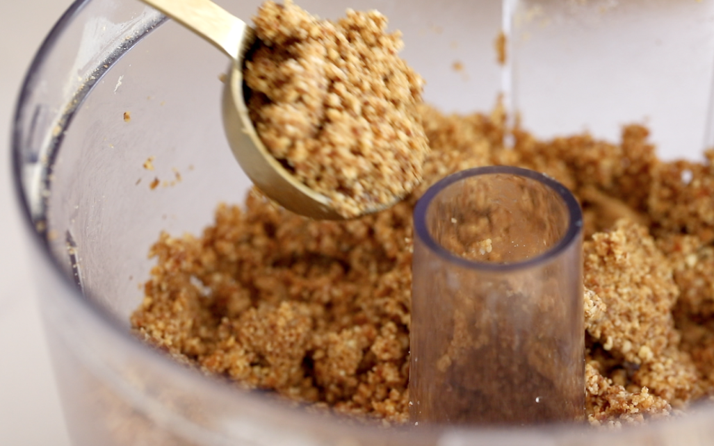 A gold spoon scooping bliss ball mixture out of a food processor.