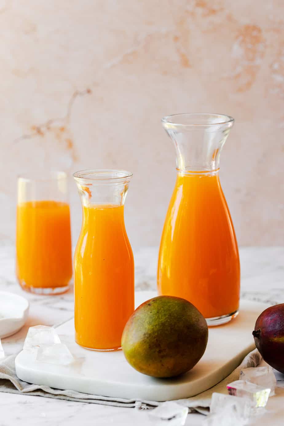 three jugs filled with juice and a fresh whole mango on marble