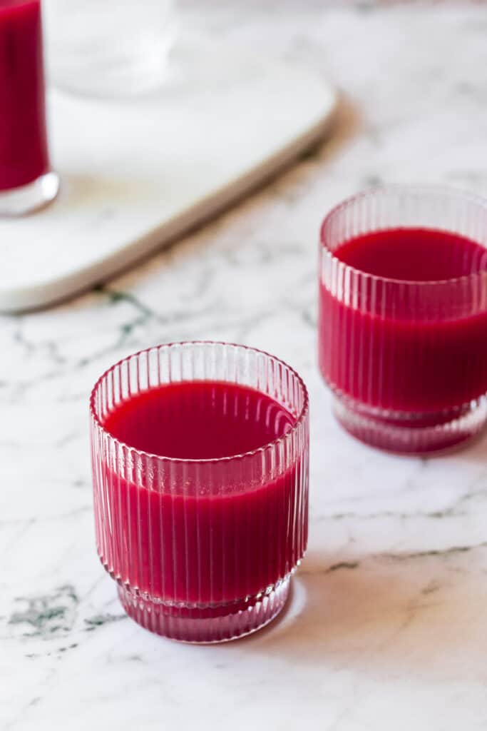 Fresh squeezed carrot and beet juice on marble background in glasses