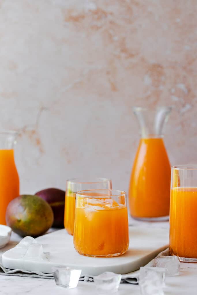 three glasses and a jug filled with juice and fresh whole mangoes
