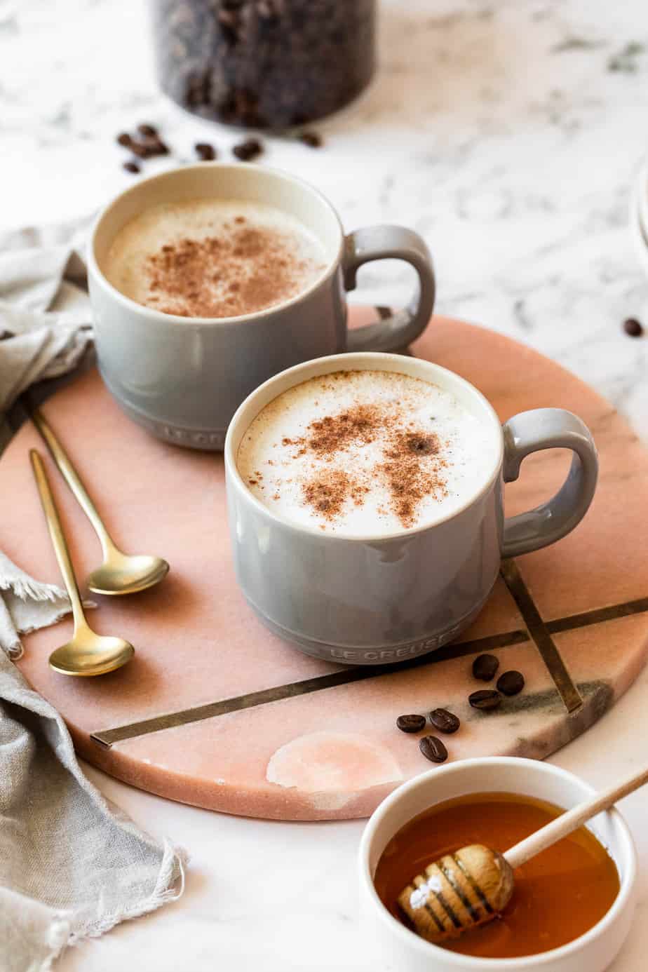 honey oat milk latte on pink marble with gold spoons