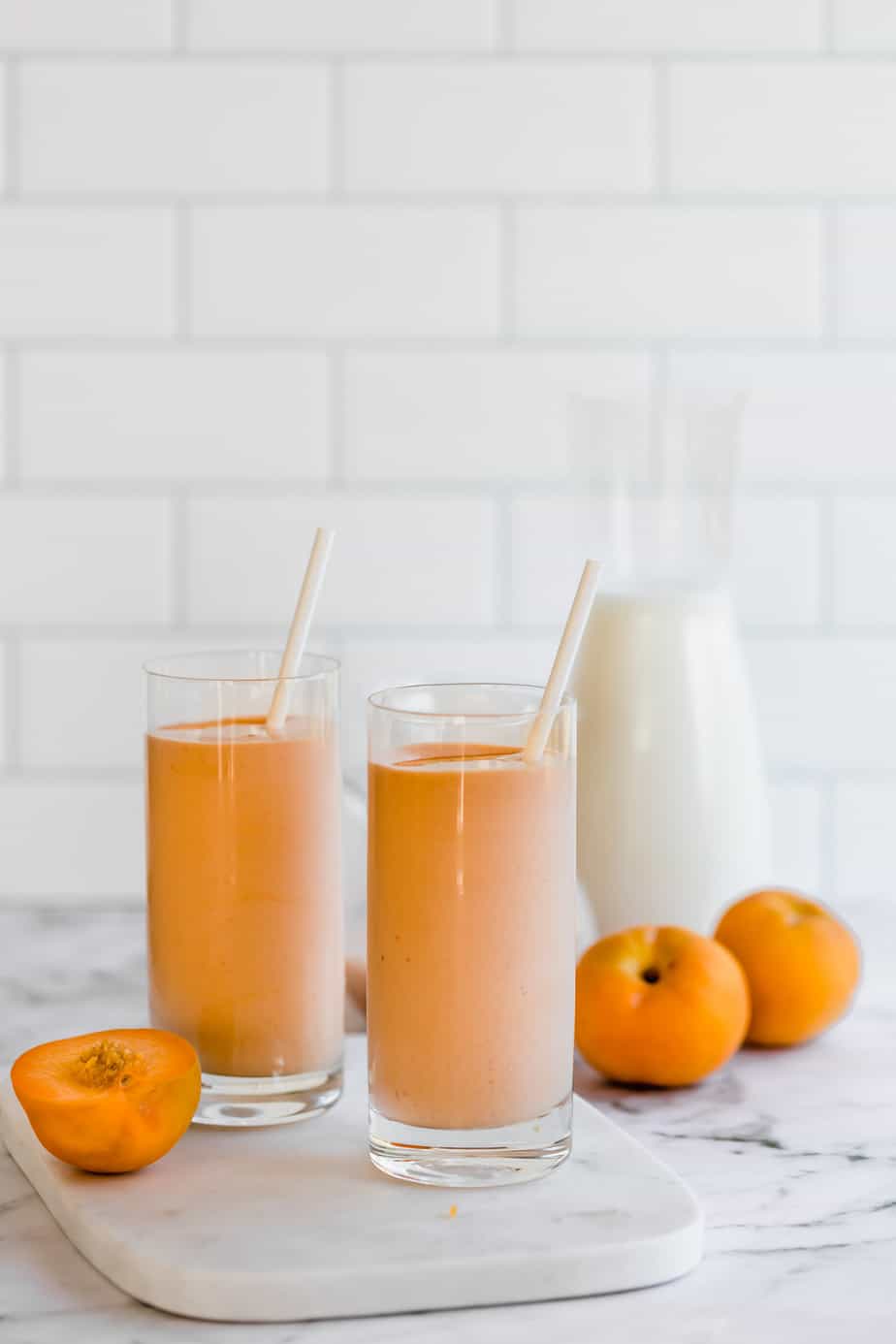 two tall glasses with smoothie and fresh peaches