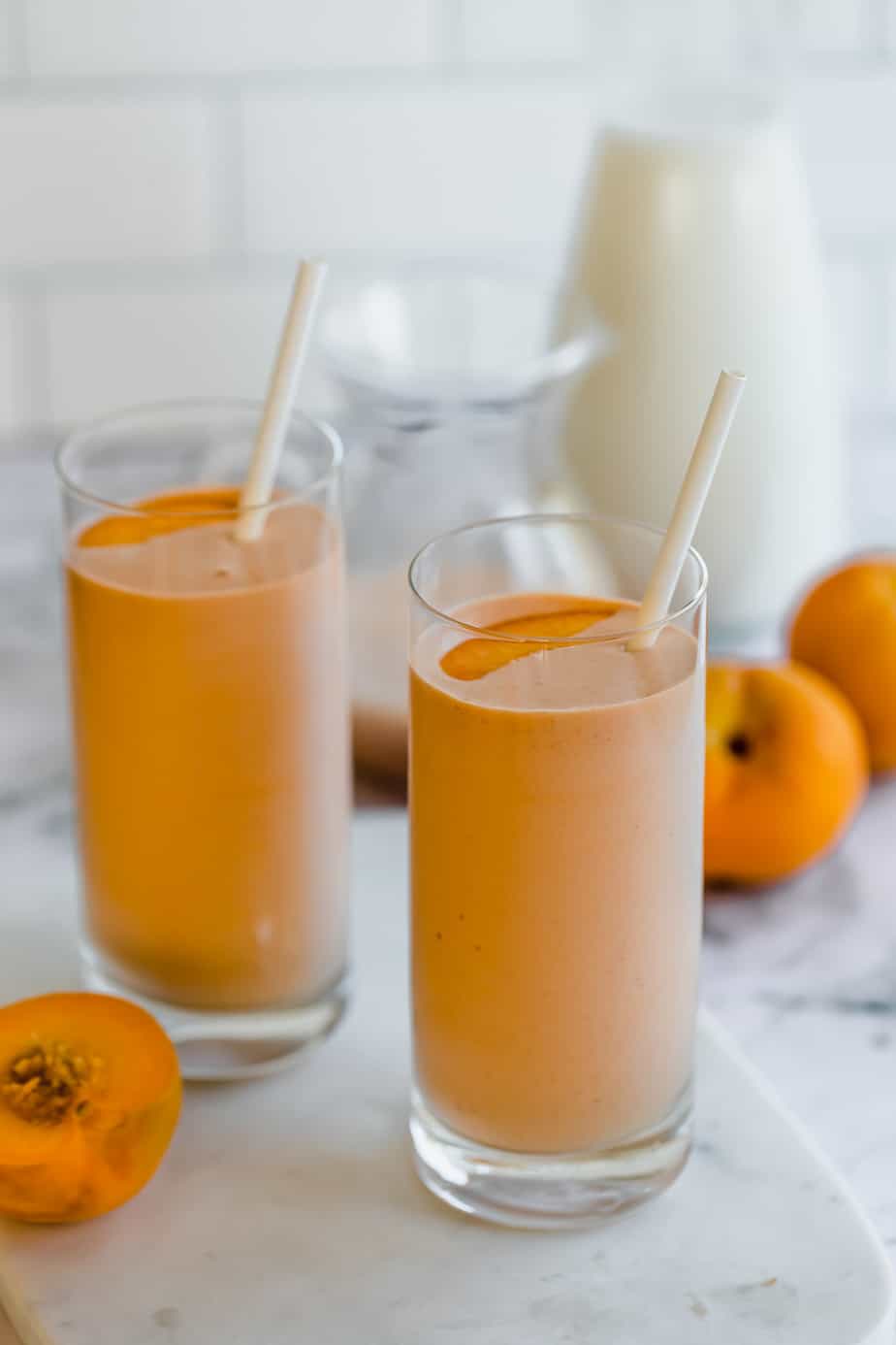 banana peach smoothie in tall glasses with straws and fresh whole peaches 