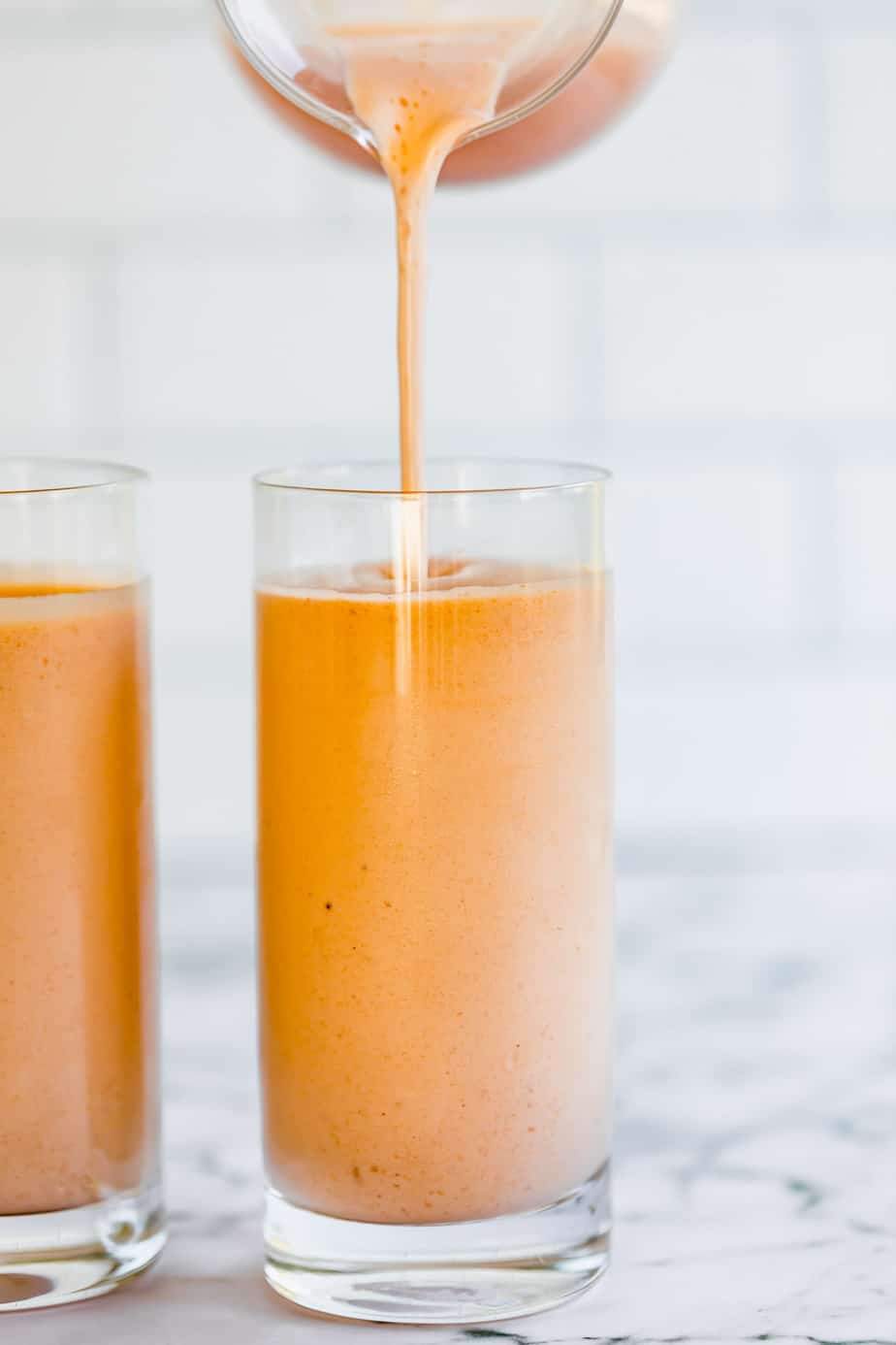 banana peach smoothie in tall glass with white tiled background