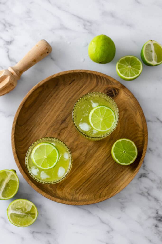 round wooden board with two glasses and limes