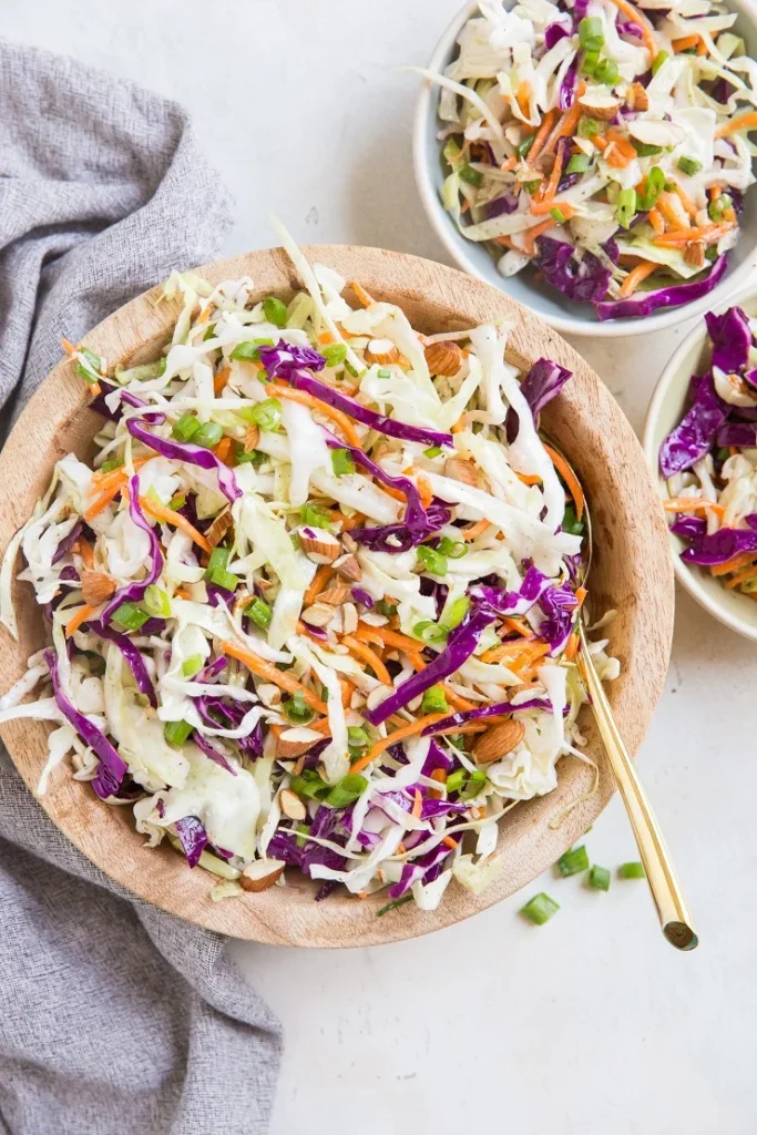 A wooden bowl of coleslaw with a gold spoon to serve it with.