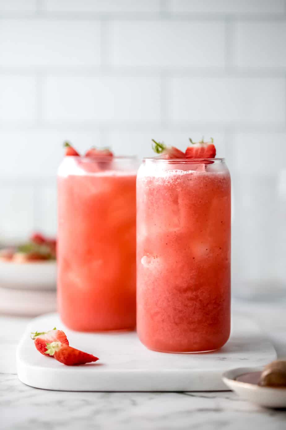 Strawberry drinks on marble with fresh strawberries cut in half.