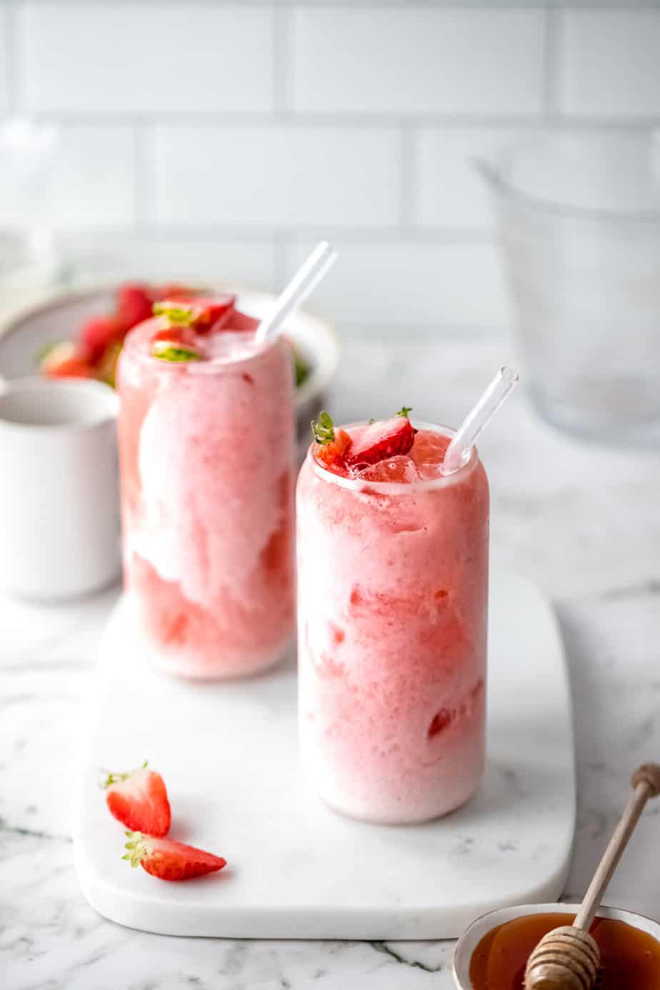 Two glasses of Agua De Fresa Con Leche with a glass straws and fresh strawberries.
