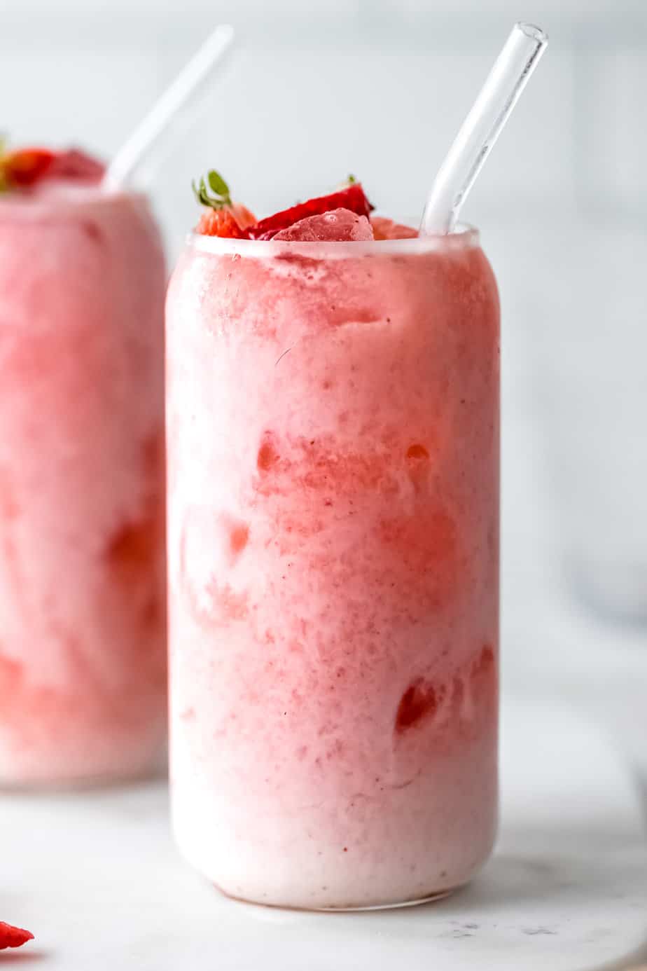 A glass of Agua De Fresa Con Leche with a glass straw and fresh strawberries.