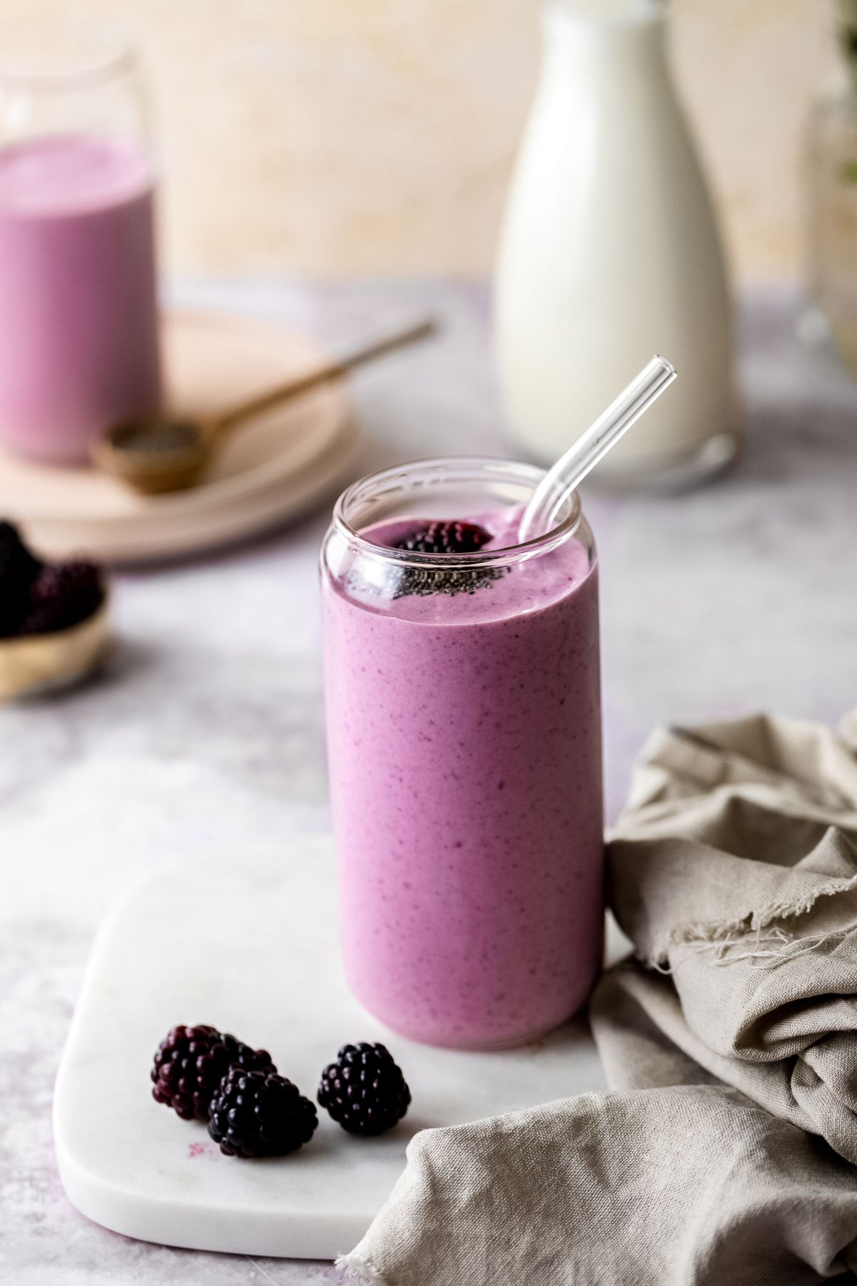 A blackberry smoothie in a serving glass with a glass straw