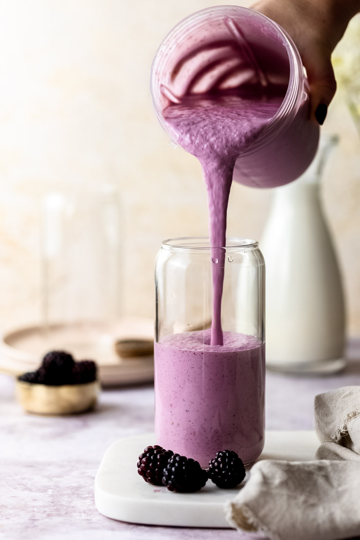 A banana and blackberry smoothie being poured into a serving glass.