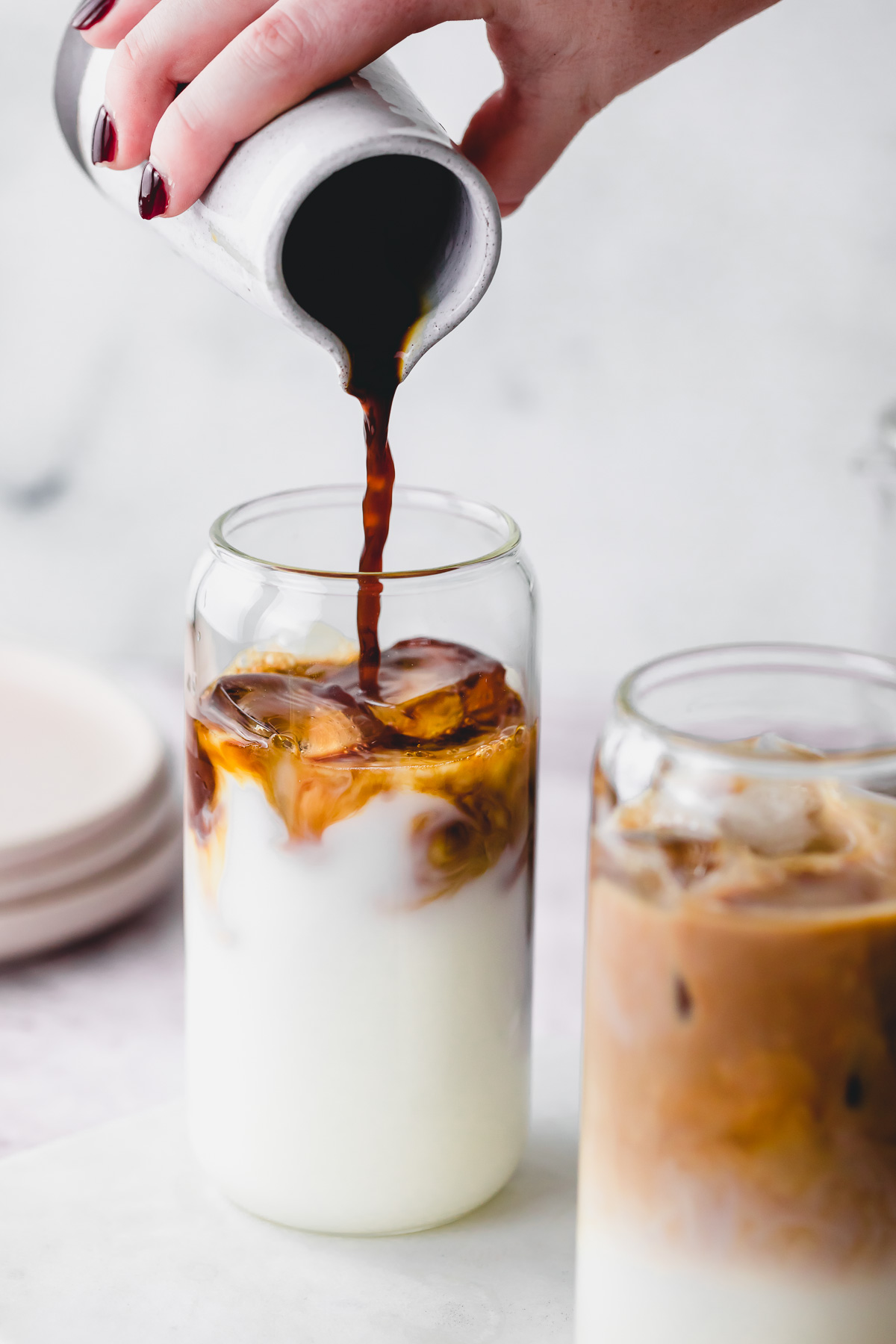 Cold brew coffee being poured into a glass of milk with ice.