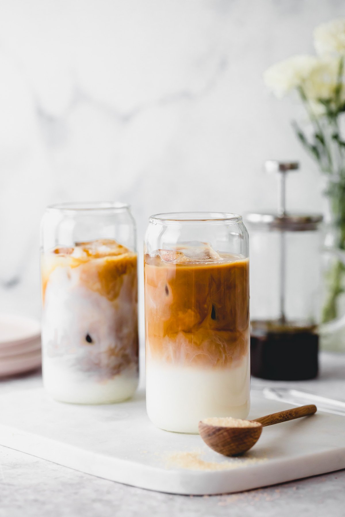 Two decaf cold brew iced coffees in tall serving glasses on white marble.