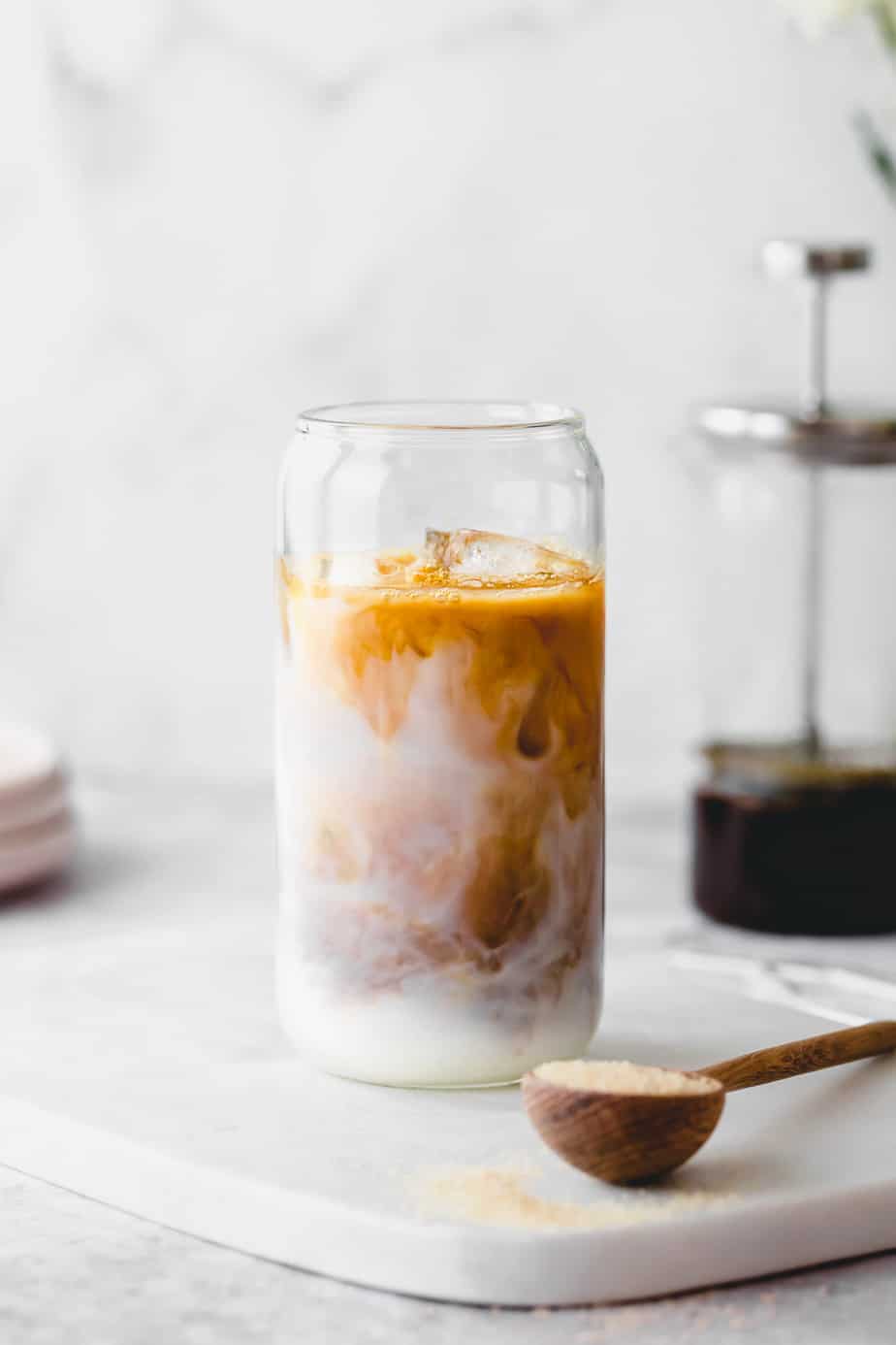 A decaf cold brew iced coffee in a glass serving glass on white marble with a spoon of brown sugar.
