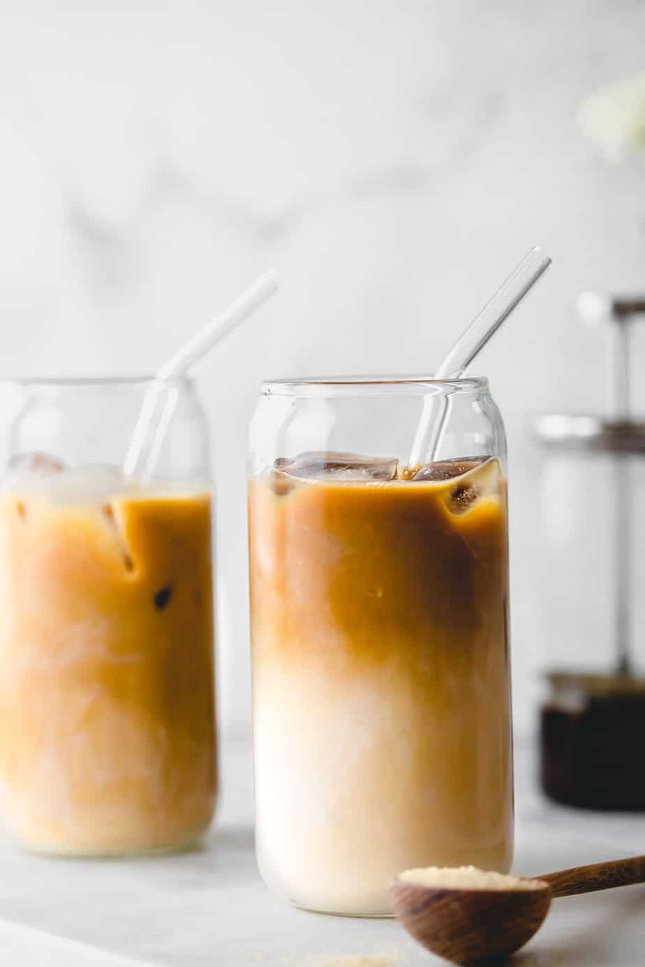 Two decaf cold brew iced coffees in tall glasses with glass straws on white marble.