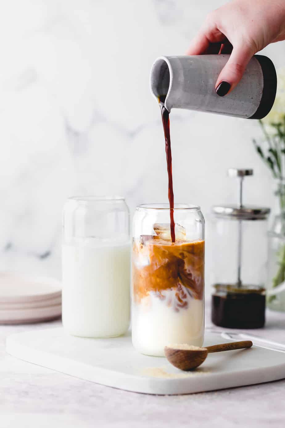Cold brewed coffee pouring into a glass of milk and ice cubes.