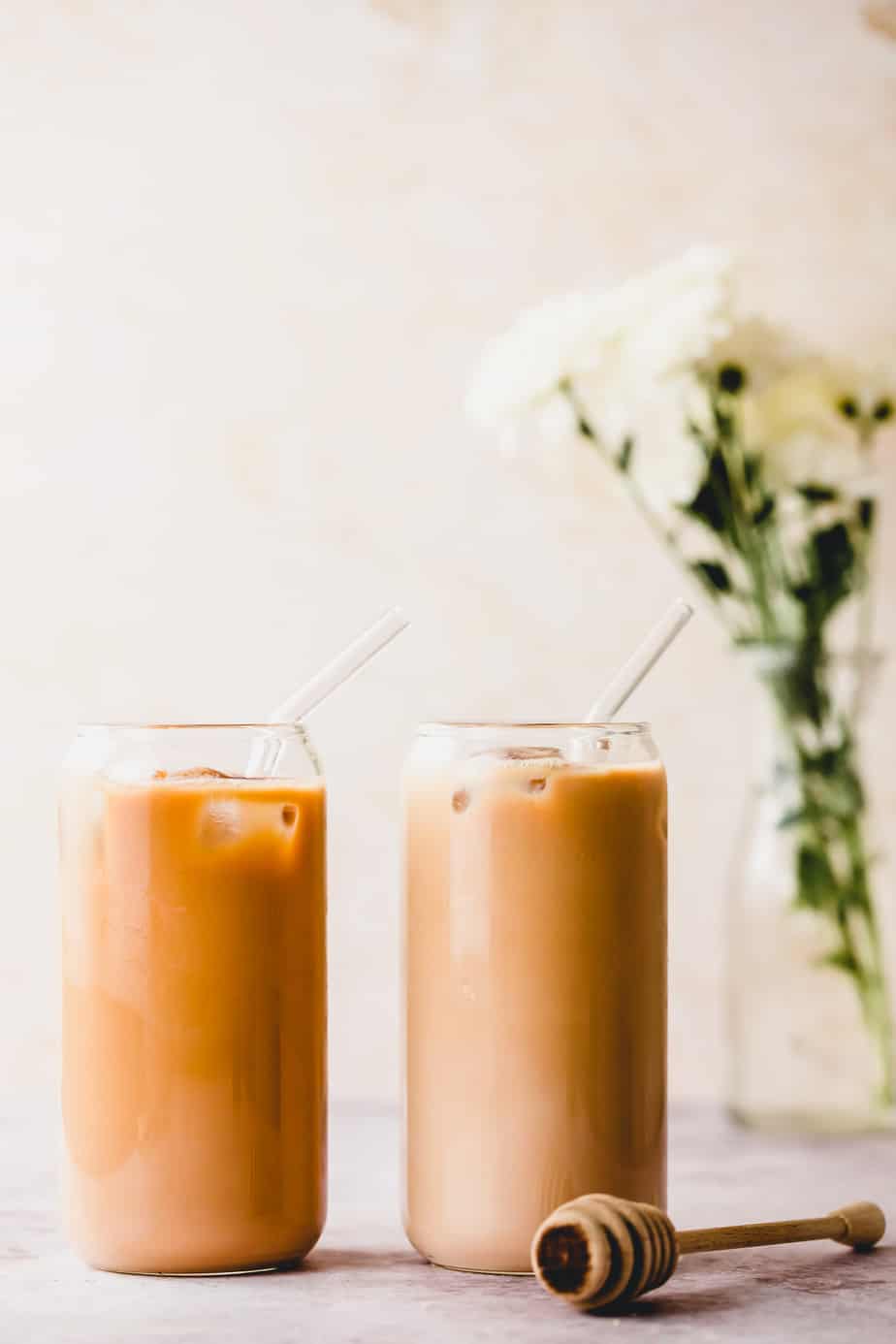 two tall glasses with honey almond milk latte and white flowers in background