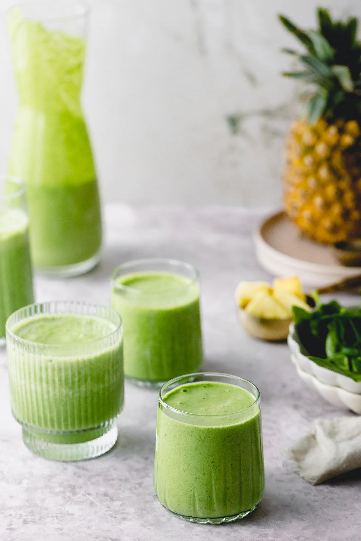 Glasses of green smoothies surrounded by fruit and spinach.