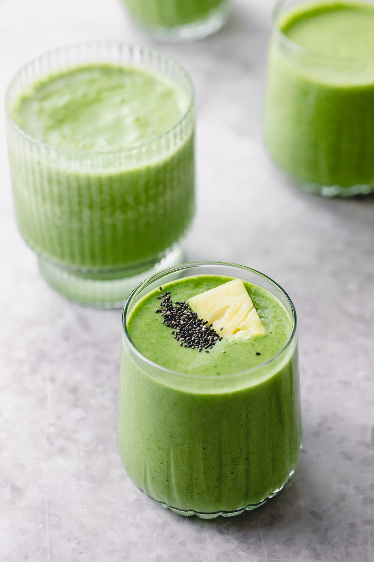 Three glasses of tropical green smoothie topped with pineapple and chia seeds.