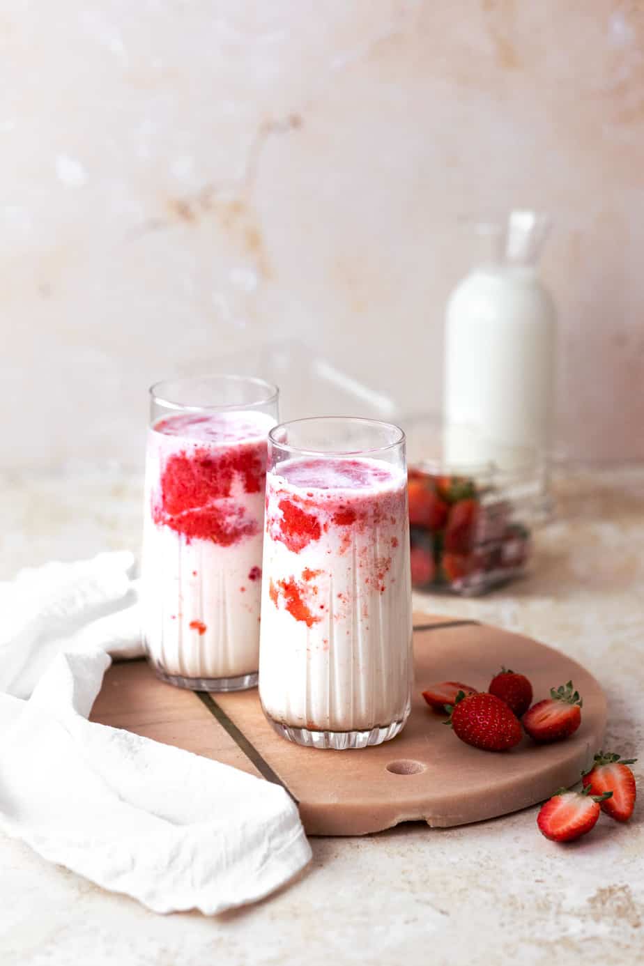 Two glasses of milk with strawberries on pink marble board.
