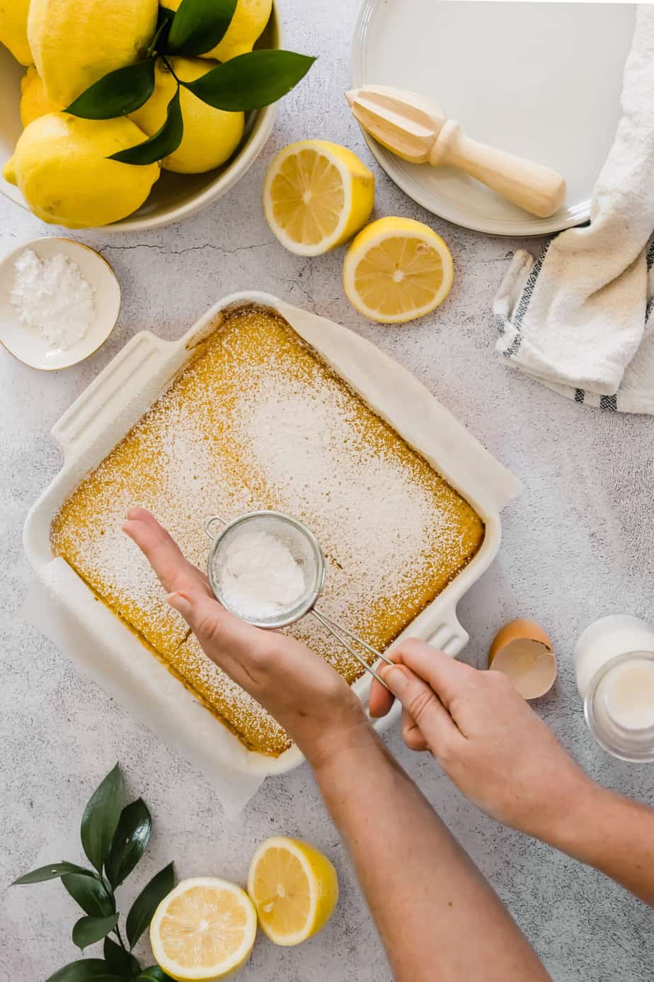 Baked lemon bars being dusted with powdered sugar.