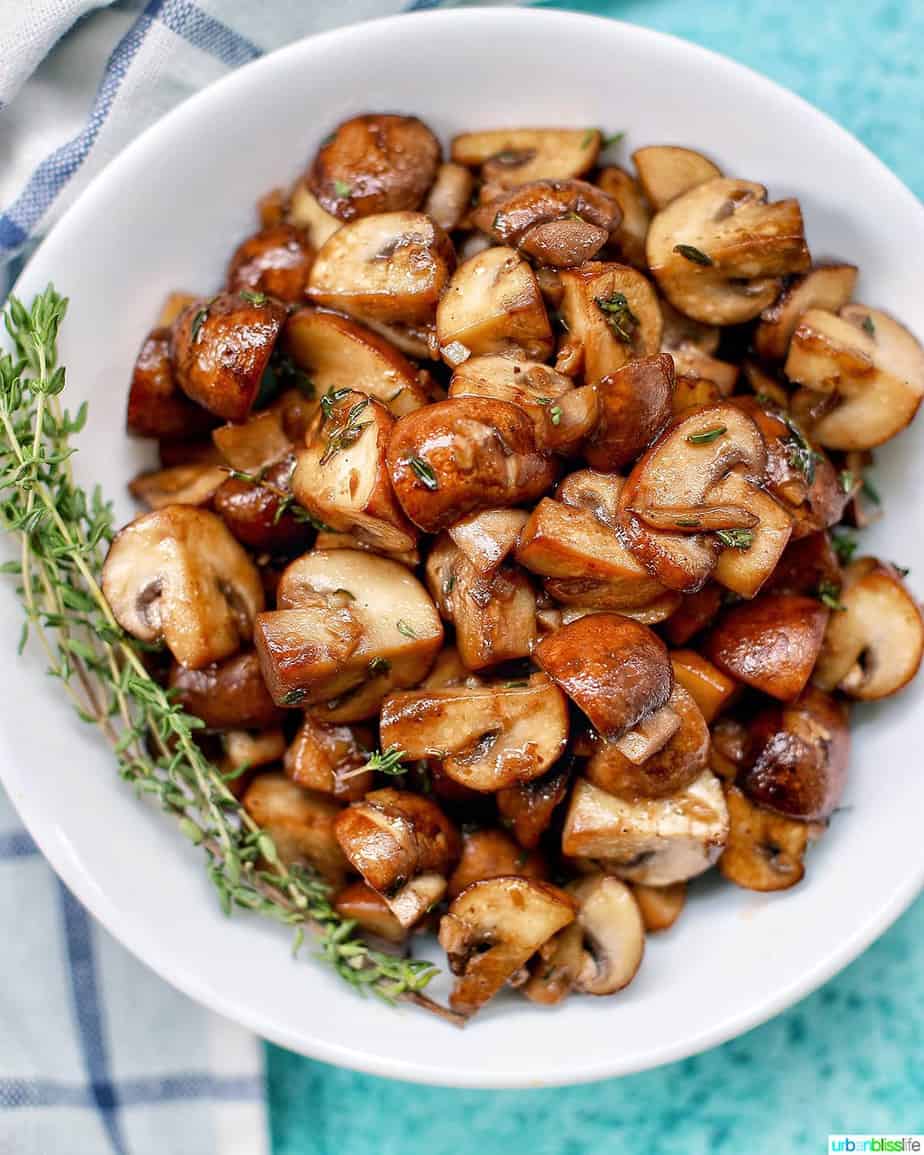 cooked mushrooms in a white bowl with fresh thyme